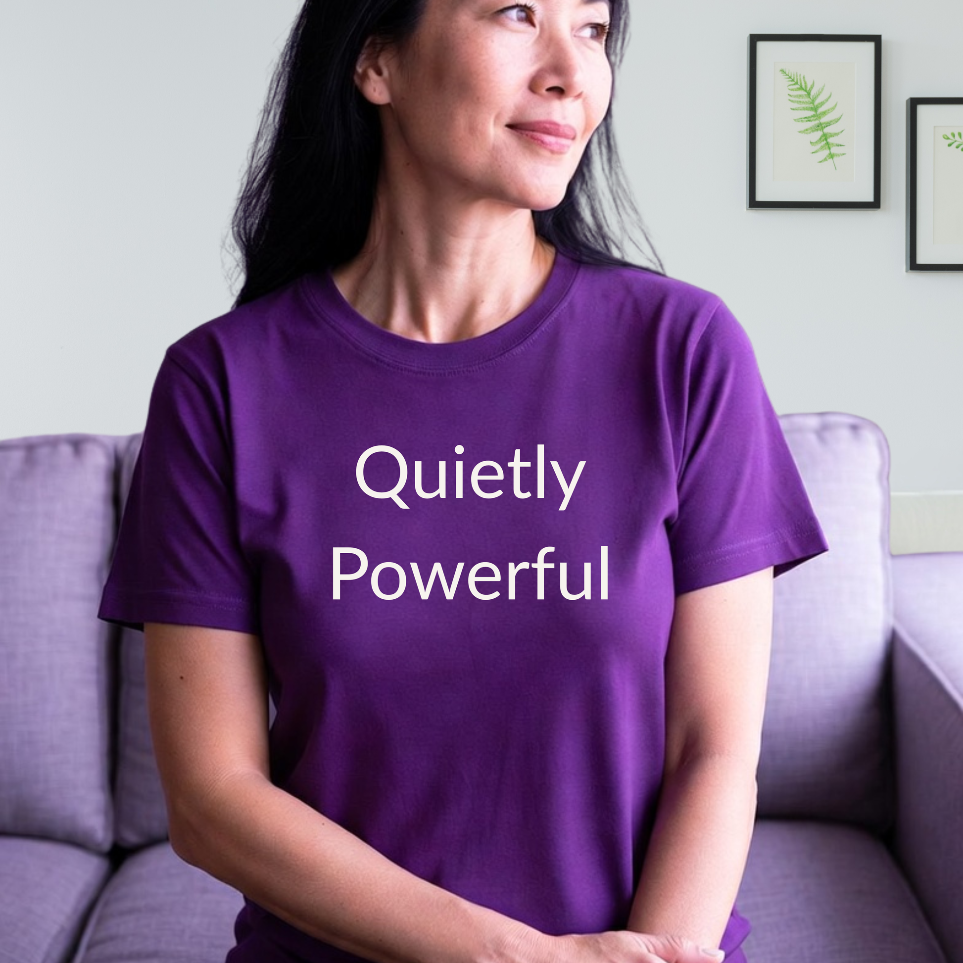 Woman wearing a purple t-shirt with 'Quietly Powerful' text, sitting on a couch.