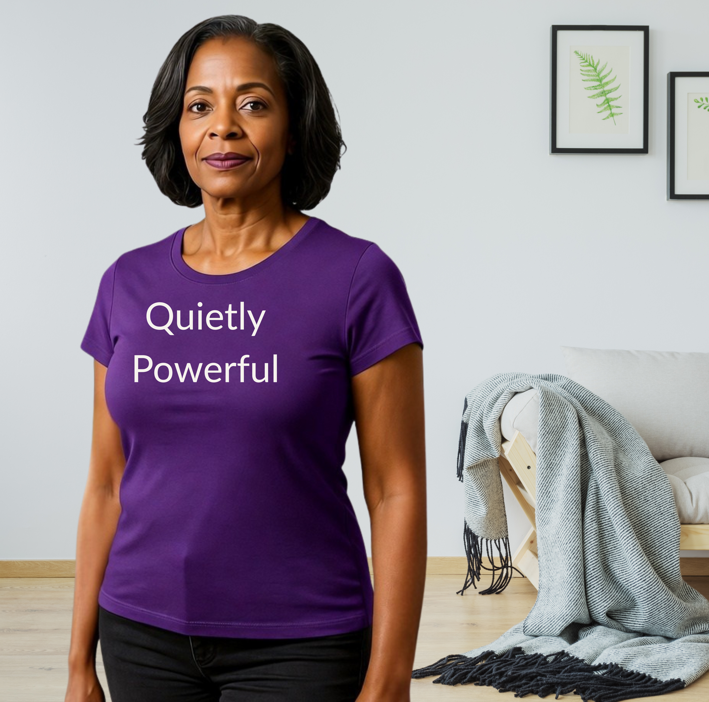 Woman wearing a purple t-shirt with 'Quietly Powerful' text in a room with a couch and blanket.