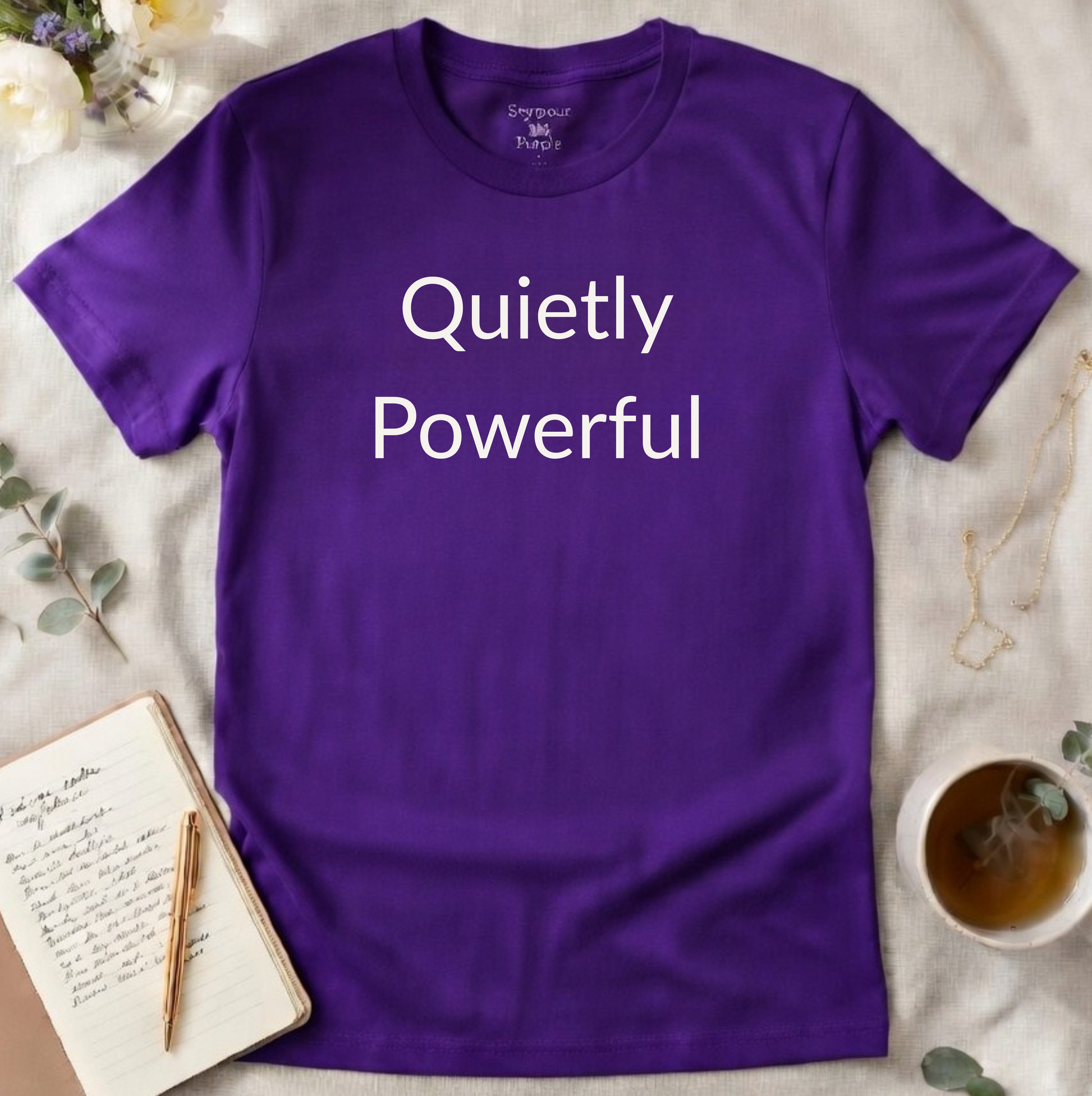 Purple t-shirt with 'Quietly Powerful' text on a light surface with decorative items.